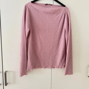Ljusrosa långärmad topp - Säljer en ljusrosa långärmad topp med vågigt strukturerat mönster. Toppen har en rak passform och är tillverkad i ett mjukt, stretchigt material som känns skönt mot huden. Perfekt för dig som gillar en enkel men ändå unik stil.