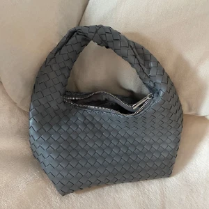 Grå flätad handväska från Gina Tricot - Snygg grå handväska från Gina Tricot med flätad design och silvrig dragkedja. 💕