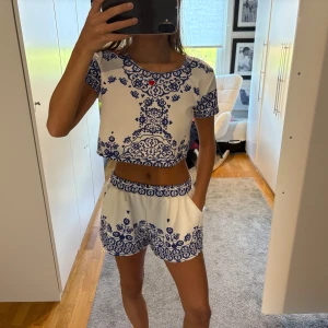 Gulligt blå/vit set - Säljer ett par vita shorts med blått, detaljerat mönster och elastisk midja. Shortsen har fickor på sidorna och en relaxed fit med en matchande tröja till!