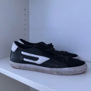 Diesel Skor - Snygga svarta sneakers från Diesel med vit logodetalj på sidan och vit häl. Skorna har snörning, platt sula och en röd undersida som ger en cool look. Bra skick! Hör av vid frågor! 👍🏼