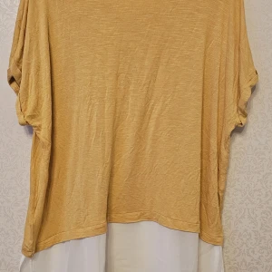 Gul  och vit blus med v-ringning - Säljer en oversized blus i gul med vit nederdel. Toppen har v-ringning, korta ärmar och en lös passform. Materialet känns mjukt och luftigt, perfekt för varmare dagar. Den har en snygg tvåfärgad design som sticker ut.