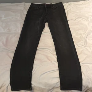 Svarta tapered jeans från Jack & Jones - Svarta jeans från Jack & Jones i modellen Tapered/Mike. Klassisk femficksdesign, raka ben med avsmalnande passform och snygga mörka sömmar. Perfekta för dig som gillar en stilren look med lite edge. Materialet är mjukt och följsamt jeans.