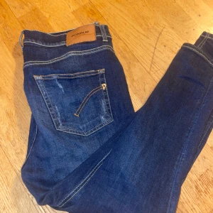 Mörkblå jeans från Dondup - Snygga mörkblå jeans från Dondup med klassisk femficksdesign och slitna detaljer framtill och på bakfickan. Jeansen har kontrastsömmar och en läderpatch med logga bak i midjan. Perfekta för en avslappnad och trendig look.