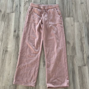 Rosa mjukisbyxor från 157 - Mysiga rosa mjukisbyxor från 157 med bred resår i midjan och dragsko. Byxorna har raka ben, stora fickor fram och bak samt är gjorda i mjukt material som känns skönt mot huden. Perfekta för chill dagar eller när du vill vara extra bekväm.