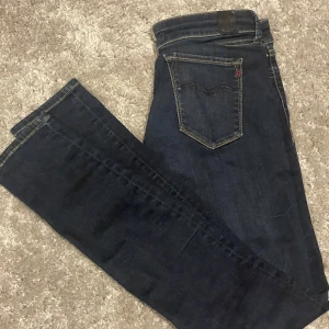 Mörkblå Replay jeans med slimfit passform  - Snygga mörkblå jeans från Replay med slimfit passform och klassiska kontrastsömmar. Byxorna har fem fickor, guldfärgade detaljer och tydlig Replay-logga vid fickan. Perfekta för dig som gillar stilrena och tidlösa jeans i denim.