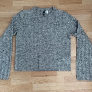 Grå stickad tröja från H&M Divided XS - Mysig grå stickad tröja från H&M Divided i storlek XS. Tröjan har ribbade detaljer, lång ärm och en klassisk rund halsringning. Materialmix med akryl, polyamid, ull, alpacka och elastan ger en skön känsla. Perfekt för kyliga dagar.