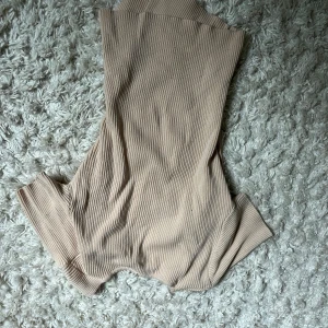 Beige ribbad polotopp från SHEIN - Säljer en beige ribbad polotopp från SHEIN. Toppen är ärmlös och har en tight passform med hög hals. Perfekt att styla med jeans eller kjol för en clean look. Materialet är mjukt och stretchigt för extra komfort.