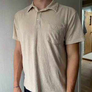 Beige frotté tröja från SNOOT - Beige pike tröja från SNOOT i mjuk frotté med klassisk krage, korta ärmar och bröstficka med broderad logga. Strlk XL. Orginalpris 900.