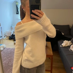 Vit offshoulder stickad tröja - Superfin vit stickad tröja med bred ribbad offshoulder-krage. Mjuk och skön, perfekt för lager på lager. Långärmad och med ribbade muddar vid ärmslut och nederkant. Enkel att styla med jeans till vintern!