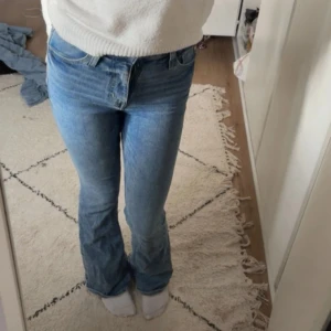 Blå bootcut jeans från &Denim - Säljer ett par klassiska blå jeans från &Denim med bootcut-modell. Jeansen har hög midja, fem fickor och är tillverkade i jeansmaterial av bomull. Perfekta för dig som gillar en retro vibe och vill ha ett par snygga utsvängda jeans i garderoben.