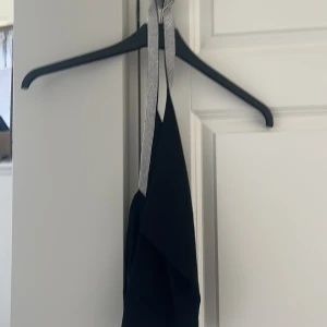 Svart festtopp med glittriga band från MNG - Supersnygg svart festtopp från MNG med glittriga axelband som ger extra bling. Festtopen har en draperad front och är axelbandslös, perfekt för att sticka ut. Materialet känns lätt och följsamt mot kroppen.