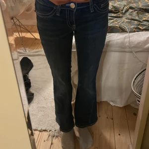 Blå bootcut jeans från Gina Tricot - Snygga blå jeans från Gina Tricot med bootcut-modell och kontrastsömmar. Jeansen har coola bakfickor med dekorativa sömmar och knappar, samt klassisk femficksdesign. Perfekta för dig som gillar en lite retro vibe och vill ha ett par jeans som sticker ut. Använda men väldigt bra skick. 🥰