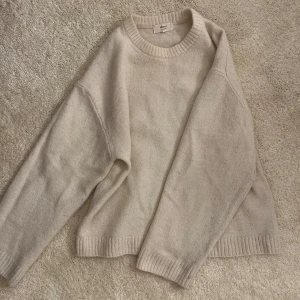 Beige stickad tröja från Gina Tricot - Mysig beige stickad tröja från Gina Tricot i ullblandning. Tröjan har rund halsringning, ribbade muddar och en avslappnad passform. Perfekt för lager-på-lager under kyliga dagar.