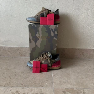 Valentino Garavani Rockrunner sneakers - Säljer ett par Valentino Garavani Rockrunner sneakers med ikoniskt kamouflagemönster. Skorna har detaljer i mocka, skinn och textil samt röda partier på hälen. Klassisk snörning och robust sula. Kommer med originalkartong och tillbehör. 100% ÄKTA Jättebra skick Nypris 5000-6000kr stl 37 men passar 38