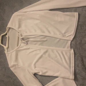 Vit croppad kofta med knyt - Säljer en vit, croppad kofta med långa ärmar och snygg knytning framtill. Perfekt att slänga över en topp för en chill och trendig look. Materialet är mjukt och lätt, vilket gör den skön att bära under vår och sommar.