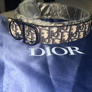 CD bälte  - Snyggt bälte med  ikoniskt CD-spänne i svart. Bältet har ett beige och svart mönster med D1or-logga över hela bandet. Perfekt accessoar för att lyfta din outfit med en lyxig touch. Dustbag medföljer!