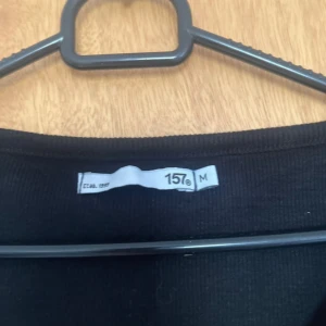 Svart croppad topp från 157 - Svart croppad topp från 157 med v-ringning och korta ärmar. Toppen har ribbad struktur och vågiga kanter vid ärmslut och nederkant för en söt touch. Perfekt att matcha med jeans eller kjol för en chill look.