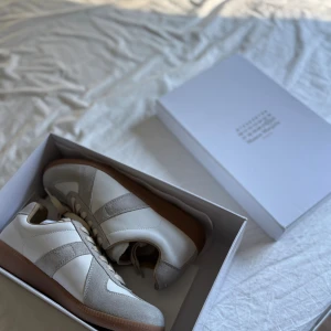 Maison Margiela Gats - Maison Margiela Gats i beige och vitt skinn och mocka, med klassisk gummisula och snörning. Snygg retrostil med diskreta detaljer och ikonisk sula med präglad logotyp. Perfekta för dig som gillar minimalistisk och clean look.