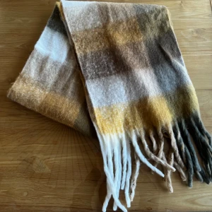 Rutig ullhalsduk  - Mjuk och fluffig halsduk med rutigt mönster i brunt, beige, vitt och gult (liknande acne studios). Långa fransar i ändarna ger en avslappnad vibe. Perfekt att svepa runt halsen för extra värme under kyliga dagar. 240cm i längd, och 40cm bred.