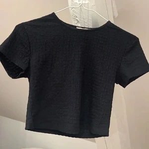 Svart croppad topp  - En snygg croppad topp med strukturerat tyg som ger en cool känsla. Perfekt att matcha med höga jeans. Helt oanvänd🩷
