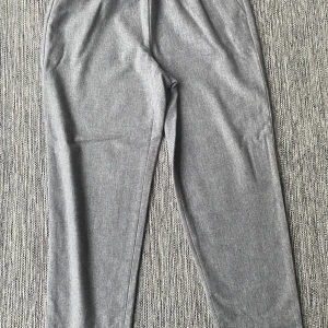 Grå tapered byxor från Eileen Fisher - Snygga grå byxor från Eileen Fisher i storlek M. De har elastisk midja och ett tapered snitt som ger en chill och modern look. Materialet känns mjukt och är troligen en blandning av ull och syntet, perfekt för dig som gillar stilrena och bekväma plagg. Mått Midjan: ca 44 cm Längd från grenen och ner: ca 72 cm  100% ull  Kommer från ett djur och rökfritt hem.