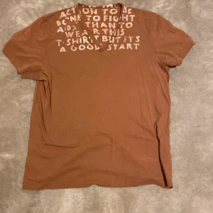 Brun t-shirt med tryck från Margiela - Brun t-shirt från Margiela, designad av Miss Deanna. T-shirten är tillverkad i 100% bomull och har en klassisk passform med korta ärmar. Har inga kvitton men den är köpt från Aplace. Är öppen för ett lägre pris vid snabb affär. Om ni har några frågor skriv gärna!