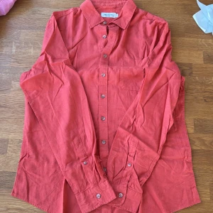 Korallröd linneskjorta Dressmann L - Snygg korallröd skjorta från Dressmann i linnemix. Klassisk krage, bröstficka och knäppning framtill. Perfekt för dig som gillar en stilren look med lite färg. Långärmad och luftig, passar grymt till jeans eller shorts. Passar M-L