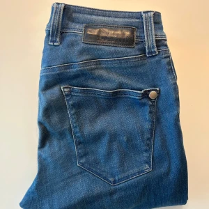 Tramarossa Jeans Slim - Säljer ett par Tramarossa jeans i blå denim. Jeansen har raka ben, fem fickor och silverfärgade nitar. Snyggt mellanblå tvätt med diskreta slitningar och Tramarossa logga på bakfickan. Perfekta för en avslappnad och stilren look.