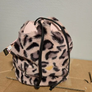 Leopardmönstrad ryggsäck med öron - Söt och fluffig ryggsäck från Top Model i leopardmönstrad pälsimitation. Väskan har svarta detaljer, snörning upptill och små rosa öron som sticker ut. Perfekt för dig som vill sticka ut med en unik och lekfull look.