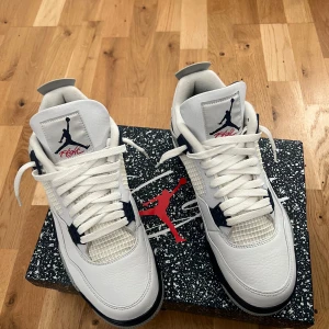Nike Air Jordan 4 Retro White/Navy - Nike Air Jordan 4 Retro i färgen White/Midnight Navy. Klassiska sneakers med vit ovandel i skinn, grå och marinblå detaljer samt stänkmönstrad mellansula. Ikonisk Jumpman-logga på plösen och hälen. Snygg siluett med snörning och meshpaneler för extra stil. Har även använt skydd till sulan och behandlat skon väl, är även öppen för andra förslag till pris.