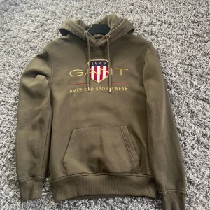 Olivgrön hoodie från GANT med tryck - Olivgrön hoodie från GANT med broderad logga och sköld på bröstet. Säljer den pga av det den är för liten.  Ny pris ca 800 säljer dne för 379!