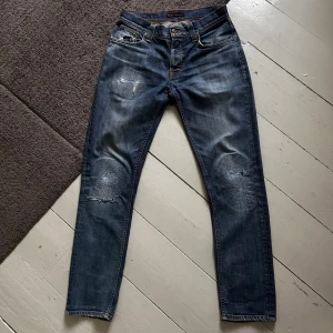 Blåa Nudie Grim Tim Jeans - Galet snygga Nudie jeans med en galant wash & stilrena slitningar i Grim Tim modell. | W31 L32 | Nypris 1699kr | Som nya, riktigt bra skick förutom ett hål vid skrevet, syns dock knappast vid användning. Kan fixas enkelt & billigt hos en skräddare. | Skriv vid minsta fundering, priset är ej hugget i sten!