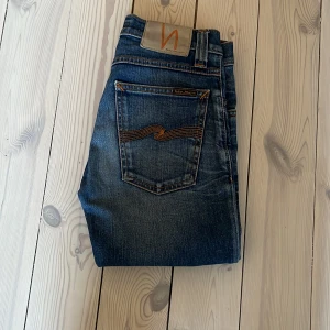 Blå jeans från Nudie Jeans - Snygga blå jeans från Nudie Jeans med klassisk femficksdesign och kontrastsömmar på bakfickorna. Jeansen har en rak passform och är tillverkade i slitstarkt denimtyg av bomull. Perfekta för dig som gillar en tidlös och avslappnad stil.