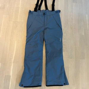 Blå termobyxor med hängslen från Everest - Som nya, använda ett fåtal gånger. Inget slitage alls. Blå termo- & täckbyxor (modell slim) från Everest med svarta justerbara hängslen och praktiska fickor. Byxorna är vadderade, vind- och vattentäta med tejpade sömmar. Byxorna är förstärkta vid knän, rumpa och benslut. Justerbar midja och snölås och knappar vid benslut. 