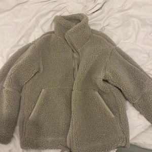 Beige teddyjacka från H&M XS - Mysig beige teddyjacka från H&M i storlek XS. Jackan har hög krage, två stora fickor framtill och stängs med dragkedja. Perfekt för kalla dagar och har en riktigt fluffig och trendig look.