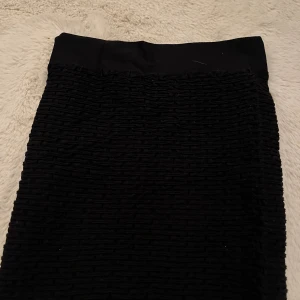 Svart ribbad kjol från Vero Moda - Svart kjol från Vero Moda i storlek S/M. Kjolen har en ribbad struktur och bred resår i midjan för en bekväm passform. Enkel och stilren design som är lätt att matcha med olika toppar och skor.