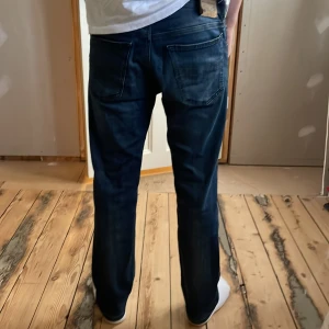 Mörkblå jeans från Diesel - Säljer ett par mörkblå jeans från Diesel med klassisk femficksdesign och snygga slitningar. Jeansen har rak passform och normal midja. Materialet är en mix av bomull och polyester med lite stretch för extra komfort. Perfekta för dig som gillar en stilren och tidlös look. 29/32