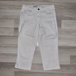 Vita capri jeans Straight Sarah - Snygga vita capri jeans från Straight Sarah i rak modell. Byxorna har fem klassiska fickor, silverfärgade nitar och en liten slits vid benslutet. Perfekta för dig som gillar en fräsch och stilren look till sommaren.