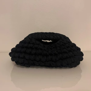 Svart och mörkblå stickad handväska med chunky look - Unik svart och mörkblå handväska med chunky, stickad design och mjukt material. Väskan har ett handtag integrerat i formen och en cool, modern siluett som sticker ut. Perfekt för dig som gillar statement-accessoarer och vill ha något annorlunda.