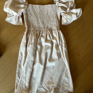 Ljus kortklänning med puffärmar - Supersöt ljus kortklänning med smockad överdel och voluminösa puffärmar. Använd 1 gång 