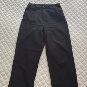 Högmidjade kostymbyxor - Snygga svarta kostymbyxor med rak och lite loose passform. Klassisk design med fickor fram och bak, bälteshällor och knappstängning. Perfekta för en clean och stilren look. Materialet känns mjukt och har en lätt glansig finish. I storlek 170 men passar för dig med storlek S-M också. Köpta från Ullared för ca 2 års sen. 