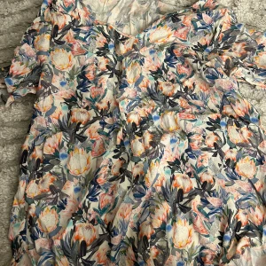 Blommig topp från H&M - Superfin topp från H&M med färgglatt blommönster i pastelliga toner av blått, rosa, orange och grönt. Klänningen har v-ringning och korta ärmar, perfekt för sommarens alla tillfällen. Lätt och luftig i bomullsmix.