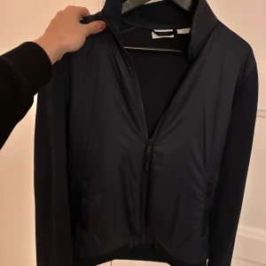 Vindjacka timberland - Snygg mörkblå vindjacka med hel dragkedja framtill och hög krage. Jackan har en stilren design och är tillverkad i ett lätt syntetmaterial som passar perfekt för blåsiga dagar. Enkel att matcha med olika outfits och har en modern passform. Köpt i USA