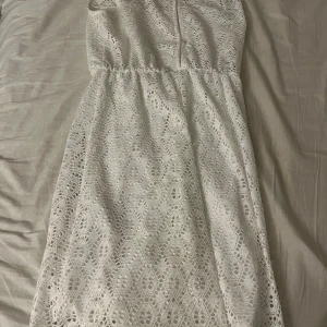 Vit spetsklänning från Fashion - Superfin vit ärmlös klänning i spets med rund halsringning och markerad midja. Klänningen har ett vackert broderat mönster och dragkedja i ryggen. Perfekt för sommarens alla tillfällen och ger en fräsch och romantisk look.Från New Yorker i storlek S