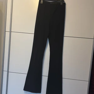 Svarta bootcut byxor från Cropp - Snygga svarta bootcut byxor från Cropp i storlek S. Byxorna har hög midja och är tillverkade i ett stretchigt tyg med diskret ribbad struktur. De har en klassisk siluett med utsvängda ben som ger en trendig look.