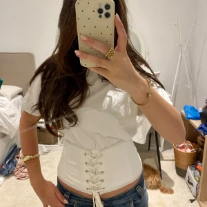 Vit korsett-topp med snörning - Supersnygg vit korsett-topp från Zara med korta ärmar och rund hals. Toppen har en unik snörning framtill som ger en cool och edgy vibe. Materialet är mjuk bomull och passformen är tight vid midjan med croppad look. Perfekt att styla med jeans eller kjol. Efterfrågad model från Zara! Pris går att diskutera!💕