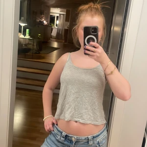 Ljusgrå croppad linnetopp - Säljer en ljusgrå croppad linnetopp med smala axelband och avslappnad passform. Perfekt för varma dagar och enkel att matcha med jeans eller shorts. Materialet är mjukt och lätt, vilket gör toppen superbekväm att bära.