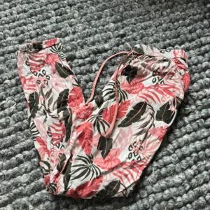 Blommiga linnebyxor från Hunkemöller XS - Snygga linnebyxor från Hunkemöller i storlek XS med tropiskt blommigt mönster i rosa, grön och vit. Byxorna har snörning i midjan och är perfekta för chill dagar. Lätta och luftiga med elastisk midja för extra komfort.