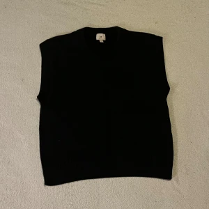 Stickad väst från H&M - Snygg svart stickad väst från H&M med v-ringad hals och ribbade kanter. Perfekt att styla över en skjorta eller t-shirt för en trendig look. Enkel och stilren design som passar till många outfits.