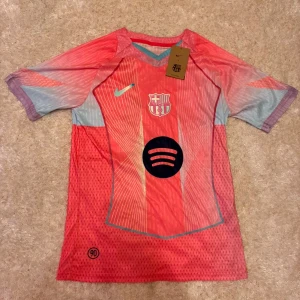 Barcelona Pedri 8 Nike fotbollströja - Säljer en Barcelona fotbollströja med Pedri 8 på ryggen, tillverkad av Nike. Tröjan har en cool rosa och ljusblå färg med vita linjer, klubbmärke på bröstet och Spotify-logga. Materialet är lätt och andas, perfekt för match eller träning.